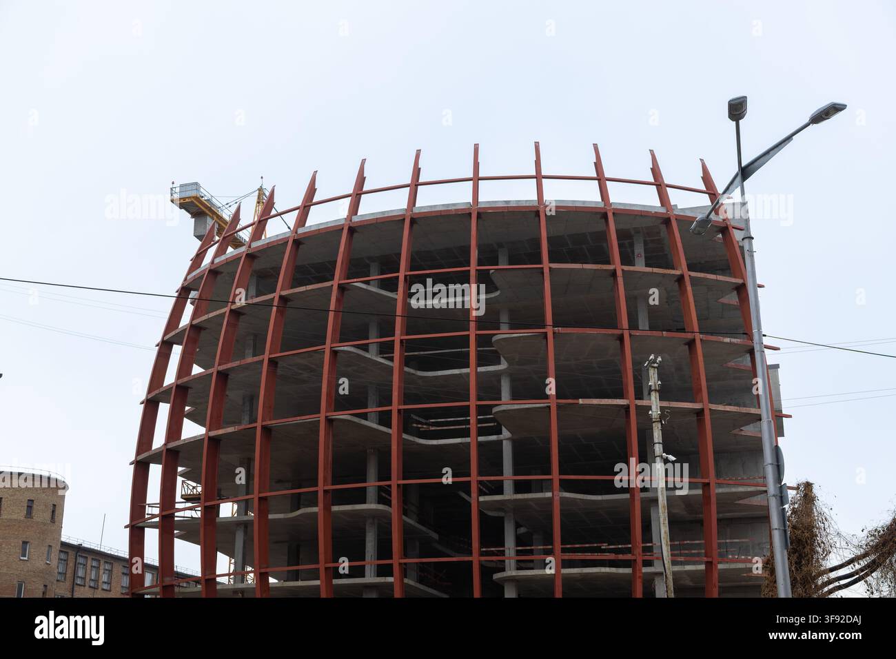 Kyiv, Ucraina - 22 marzo 2026: L'edificio ovale incompiuto mostra un'architettura moderna con travi d'acciaio scheletriche che sostengono i livelli mentre la gru equi Foto Stock