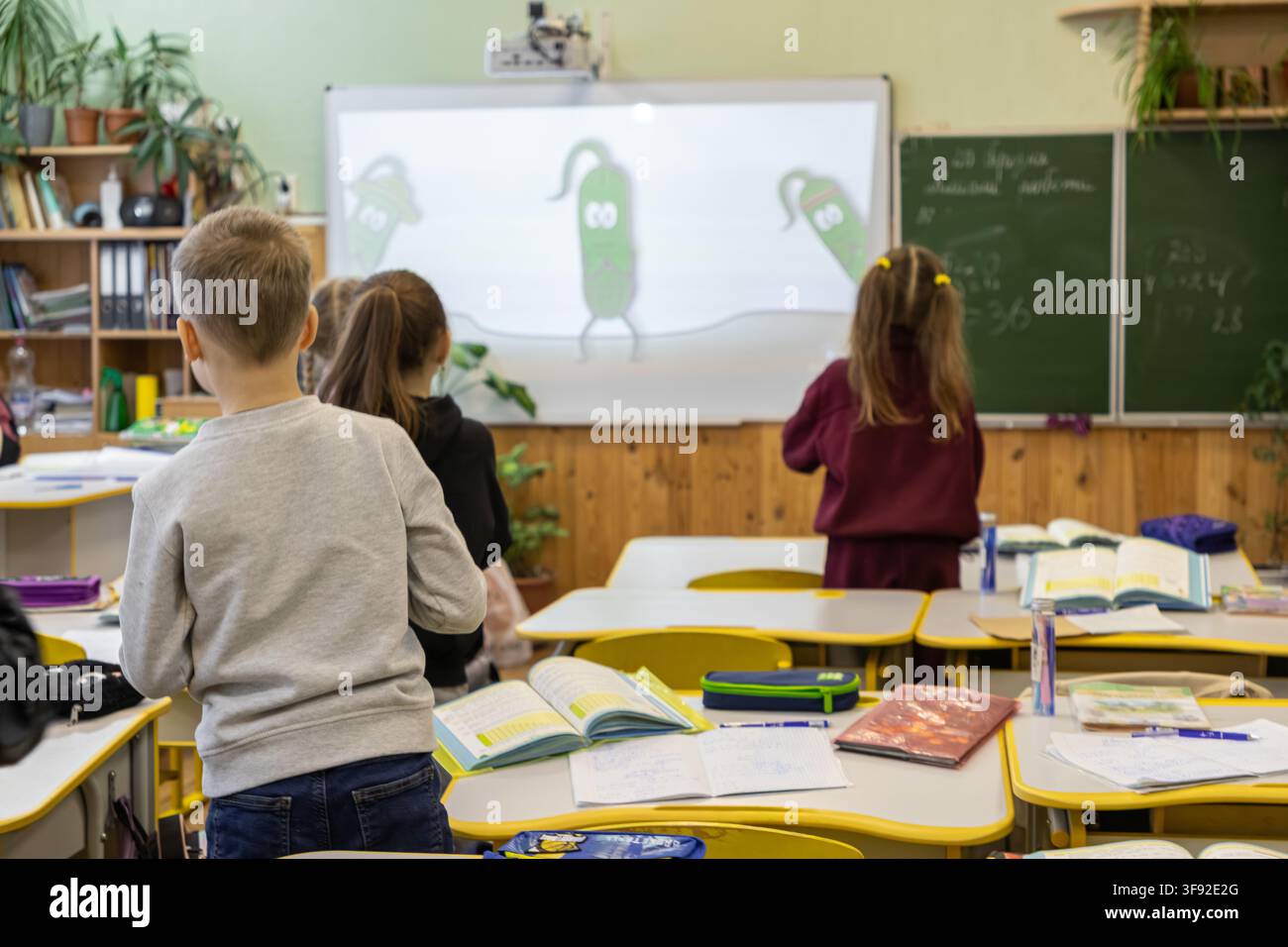 Gli studenti delle scuole primarie osservano una vivace presentazione digitale durante una lezione in classe, evidenziando un'esperienza di apprendimento interattiva in un ambiente luminoso Foto Stock