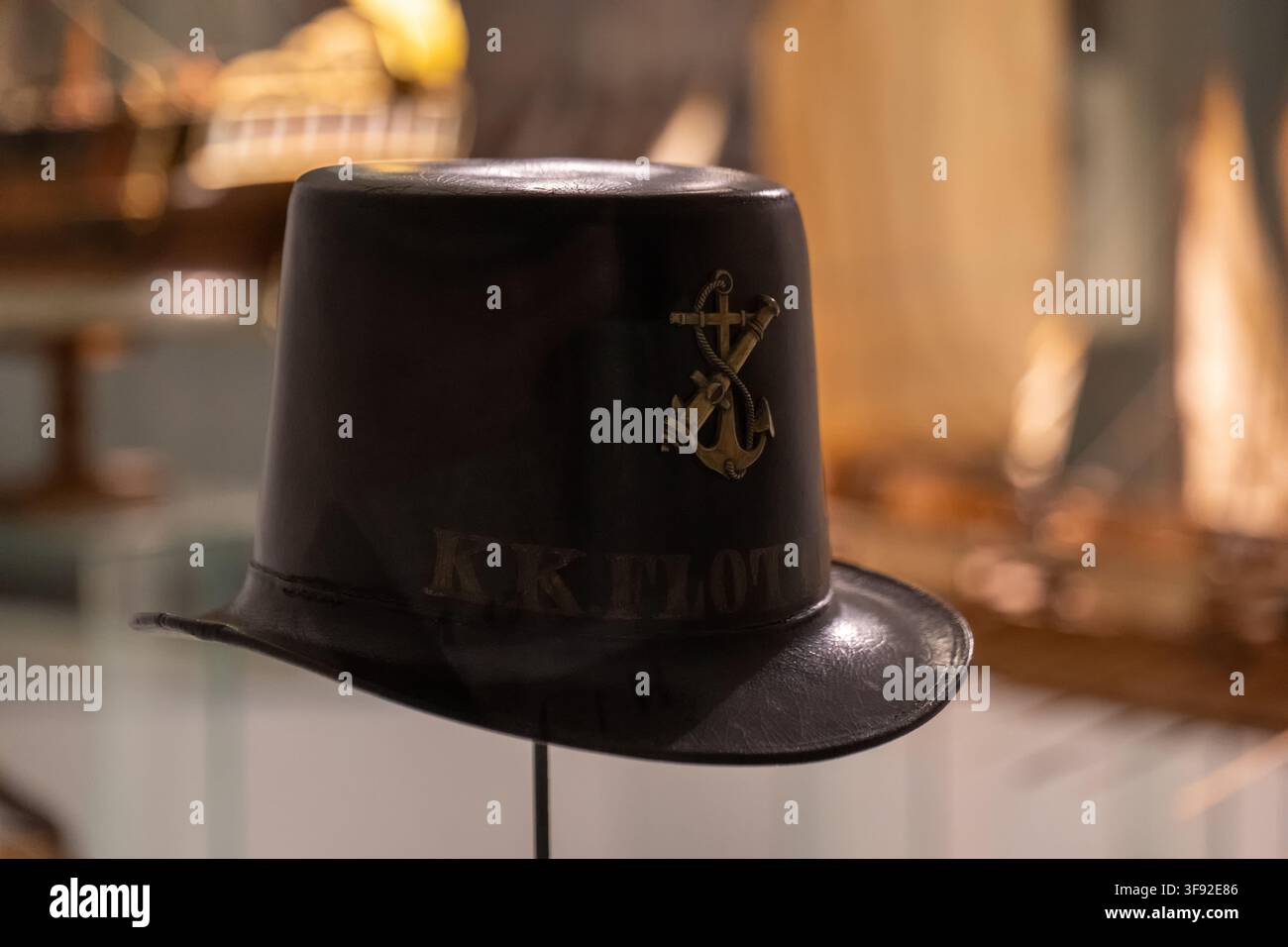 VIENNA, AUSTRIA, 13 agosto 2026: Un cappello nero con un emblema ad ancora è esposto all'interno su uno sfondo sfocato con toni caldi. Foto Stock