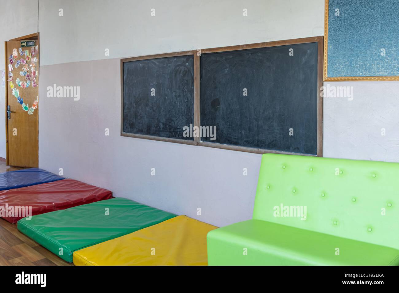 Un asilo o area di gioco dell'infanzia luminosa con pannelli lavagna vuoti, tappetini da gioco morbidi nei colori primari e sedute moderne verdi per i bambini da Foto Stock