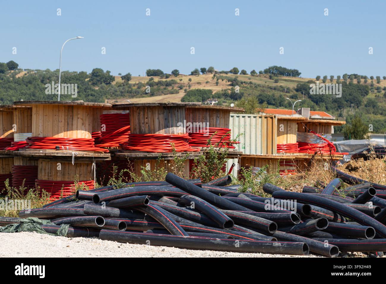 Grandi bobine di legno con cavo rosso e tubi di plastica nera sul territorio di un'installazione industriale. Foto Stock