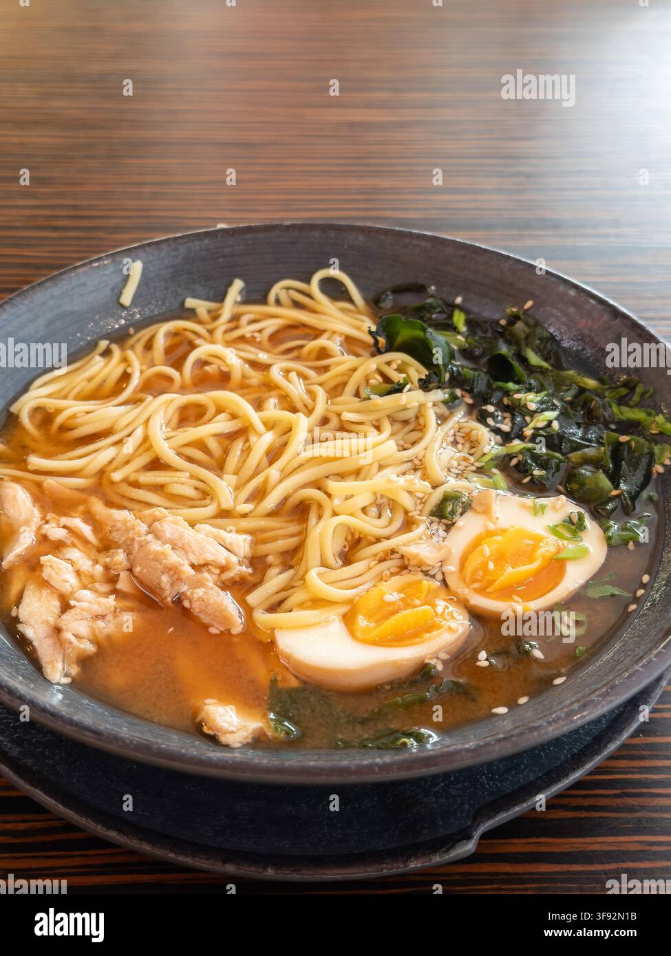 La zuppa gourmet di ramen con brodo saporito, noodles di grano elastici e semi di sesamo serviti in una ciotola di ceramica scura, evocando il calore e il comfort di un t Foto Stock