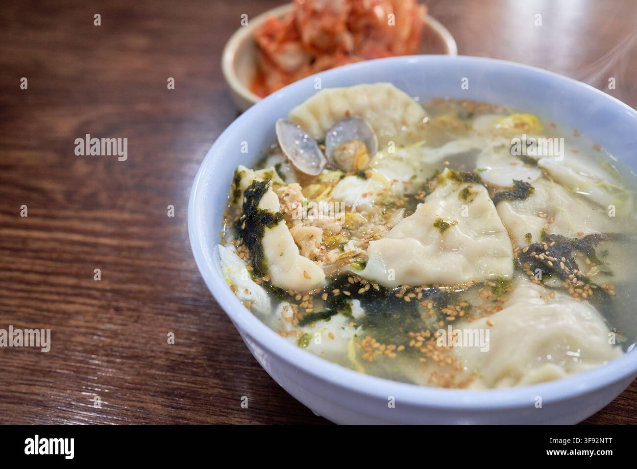 Zuppa tradizionale coreana di dumpling tteokmanduguk con torte di riso affettate, strisce di uovo e vongole servite insieme al kimchi di cavolo napa in un ristorante locale Foto Stock