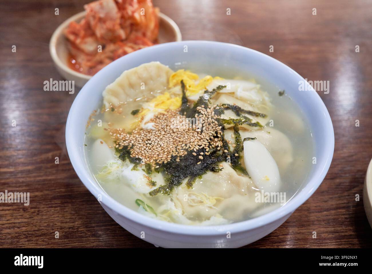 Zuppa tradizionale coreana di dumpling tteokmanduguk con torte di riso affettate, strisce di uovo e vongole servite insieme al kimchi di cavolo napa in un ristorante locale Foto Stock
