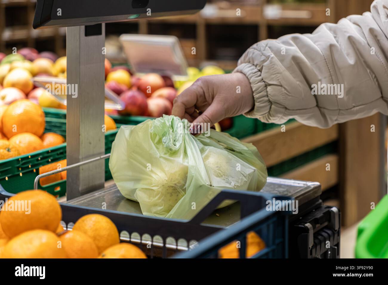 Un cliente posa una borsa piena di prodotti su una bilancia digitale in un negozio di alimentari, raffigurando l'attività comune di acquistare cibo fresco in un ambiente di vendita al dettaglio Foto Stock