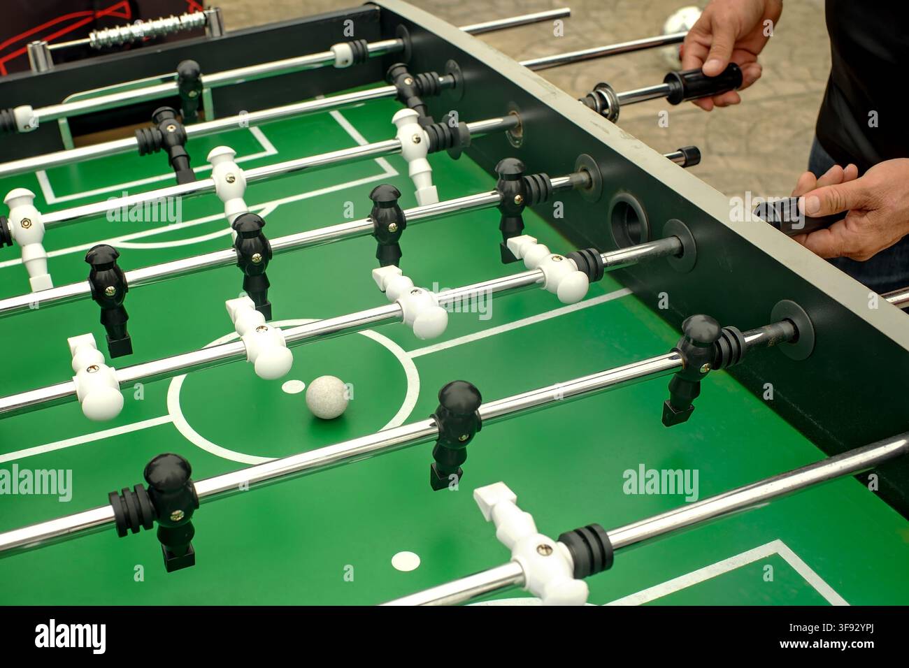 Primo piano di mani maschili che giocano a calcio da tavolo all'aperto su un tavolo verde con una palla bianca sporca e linee polverose Foto Stock