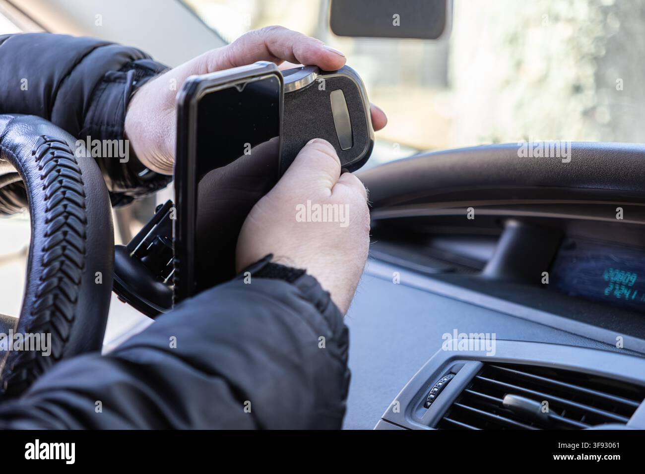 Vista ravvicinata di mani che posizionano uno smartphone in un supporto del cruscotto all'interno di un'automobile, illustrando come i conducenti utilizzano la tecnologia per gestire mappe e comunicazioni Foto Stock