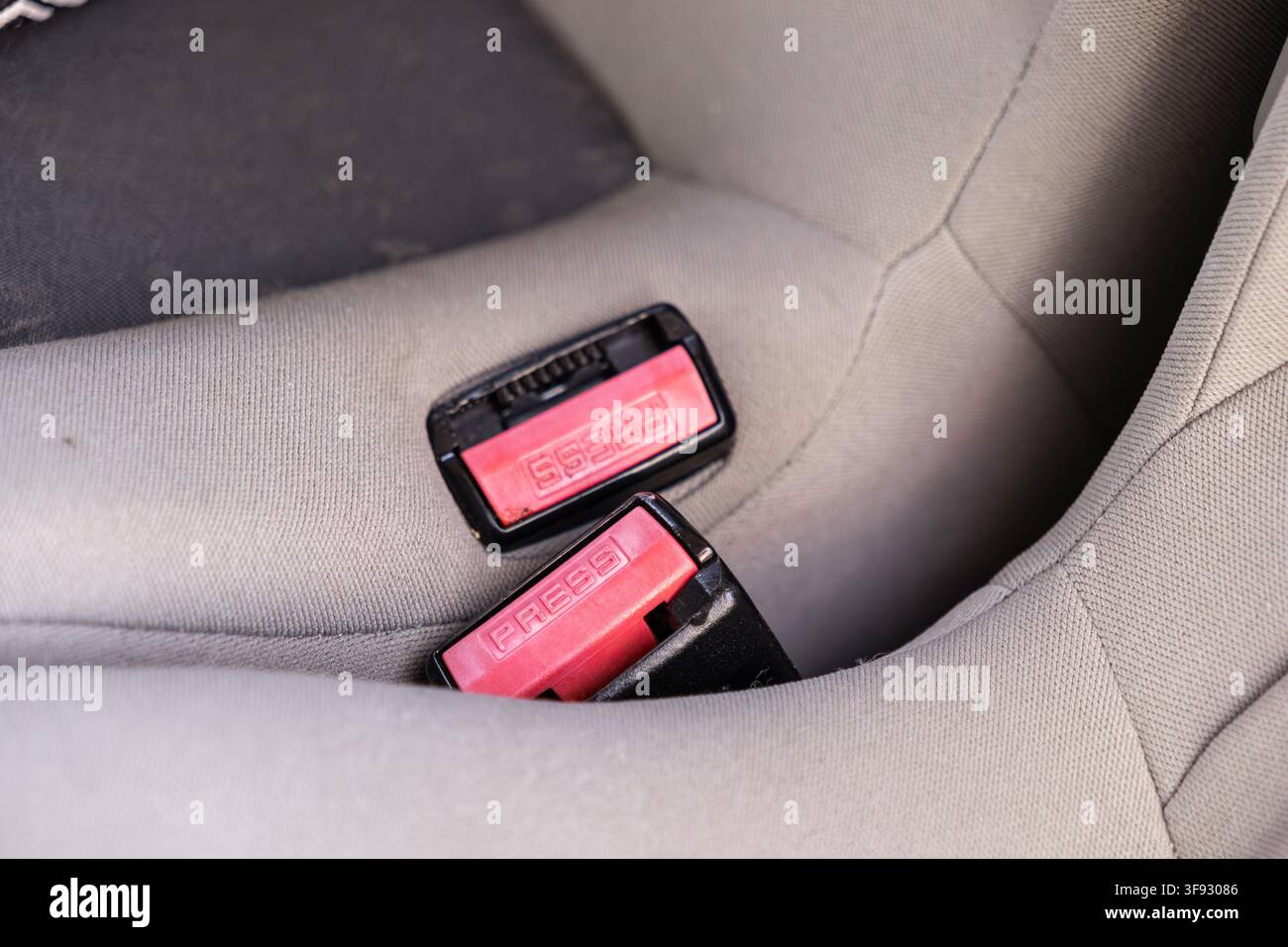 Primo piano di fibbie della cintura di sicurezza sganciate con pulsanti di rilascio rossi su un sedile auto grigio morbido, che illustra i sistemi di sicurezza per il trasporto automobilistico Foto Stock