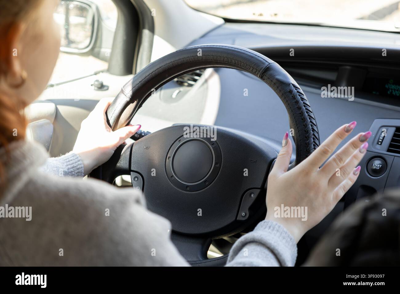 Primo piano di una conducente che tiene il volante durante una guida mattutina luminosa, simboleggiando la mobilità personale, la libertà di viaggio e la sicurezza stradale in Foto Stock