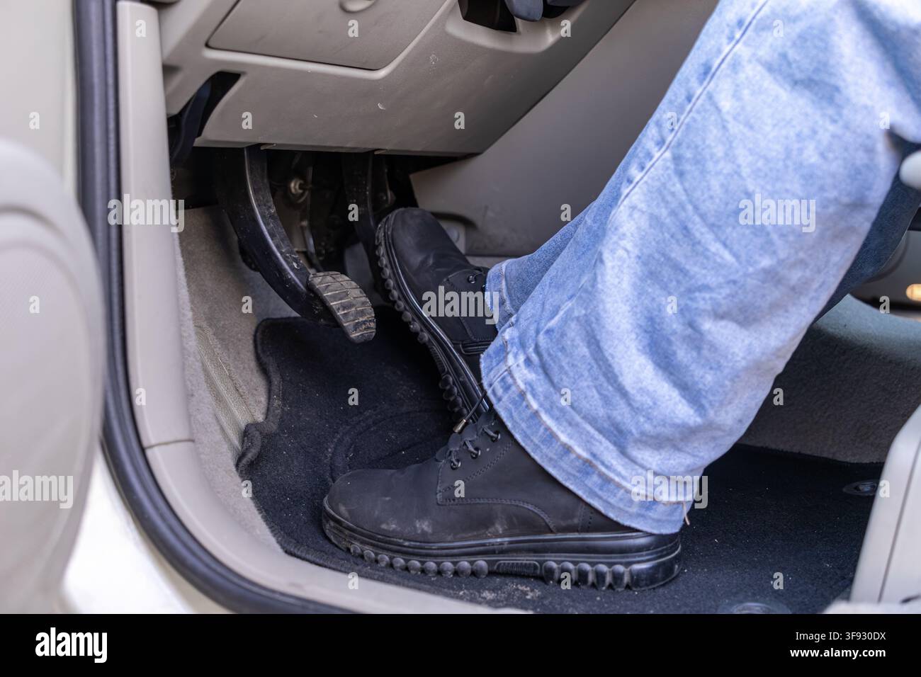 Un piede che preme il pedale del freno all'interno di un'auto evidenzia la guida difensiva e la consapevolezza della sicurezza stradale mostrando l'azione fisica precisa dell'opera Foto Stock