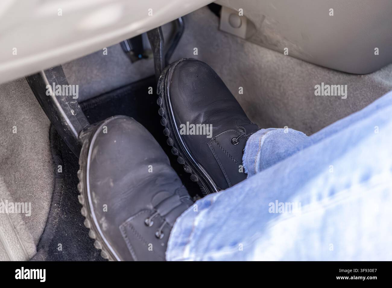 Un piede in uno stivale da lavoro resistente preme il pedale dell'acceleratore all'interno della cabina del veicolo, evidenziando l'importanza di una guida prudente e del funzionamento del veicolo Foto Stock
