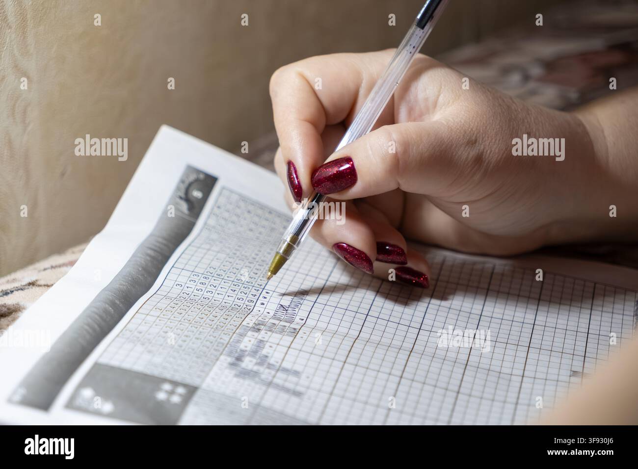 Una mano con smalto scintillante segna una griglia su un puzzle logico di carta, dimostrando concentrazione strategica, pazienza e sviluppo di abilità ricreative all'interno di una Foto Stock