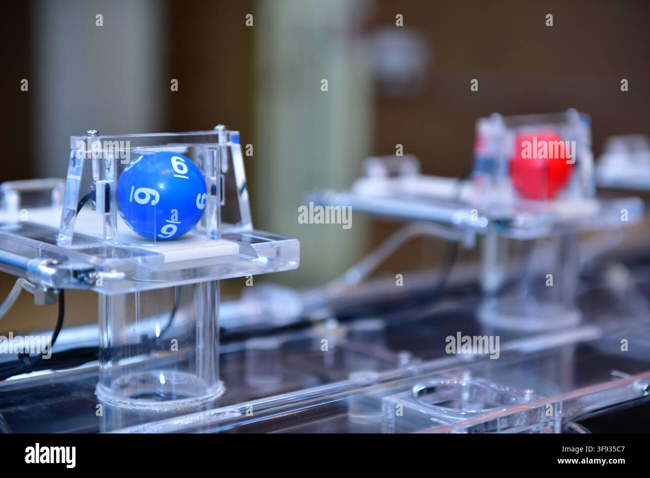 Un primo piano di una macchina per l'estrazione della lotteria con una pallina blu numerata all'interno di un contenitore trasparente. Foto Stock