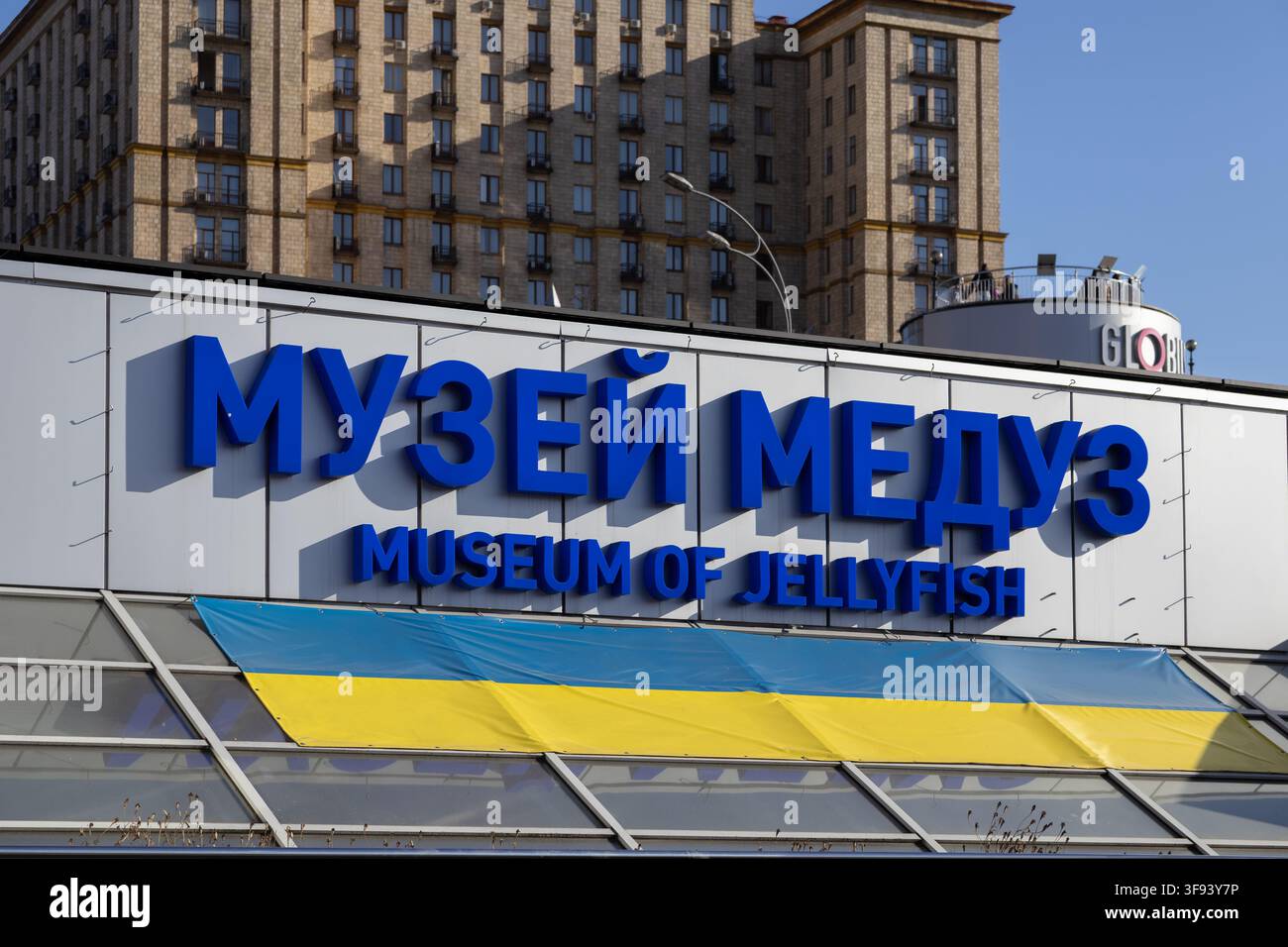 Kiev, Ucraina - 15 marzo 2026: Scritte blu audaci del Museo delle meduse su un muro grigio con una bandiera ucraina esposta all'aperto, che trasmette loca Foto Stock