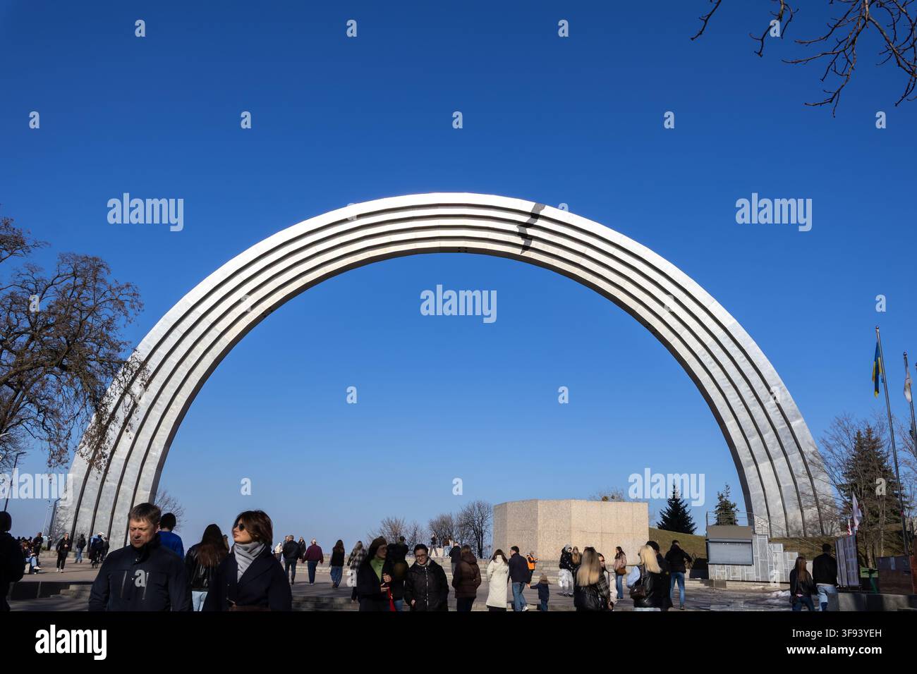 Kiev, Ucraina – 15 marzo 2026: folla che passeggia vicino all’iconico monumento in acciaio mentre i turisti godono di una giornata soleggiata nel parco pubblico, riflettendo la cultura cittadina Foto Stock