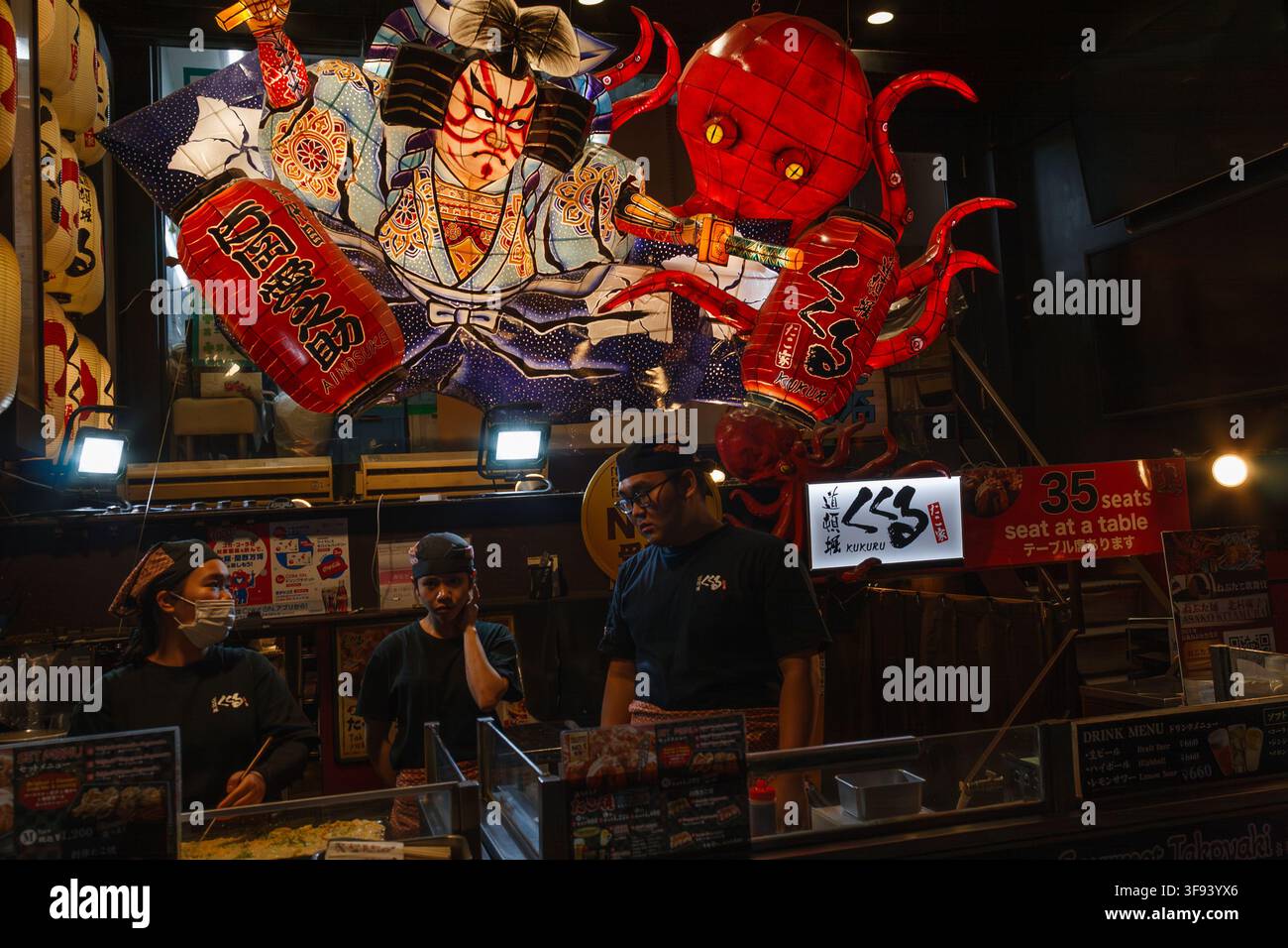 Chef che preparano street food sotto un gigantesco cartello a forma di polpo in una famosa bancarella di takoyaki a Dotonbori Osaka in Giappone. Foto Stock