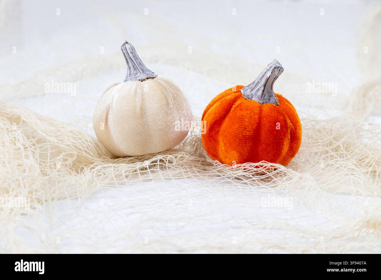 Una natura morta orizzontale a tema Halloween con due zucche di stoffa posate su un materiale bianco a ragnatela sottile. Le texture morbide delle zucche e il d Foto Stock