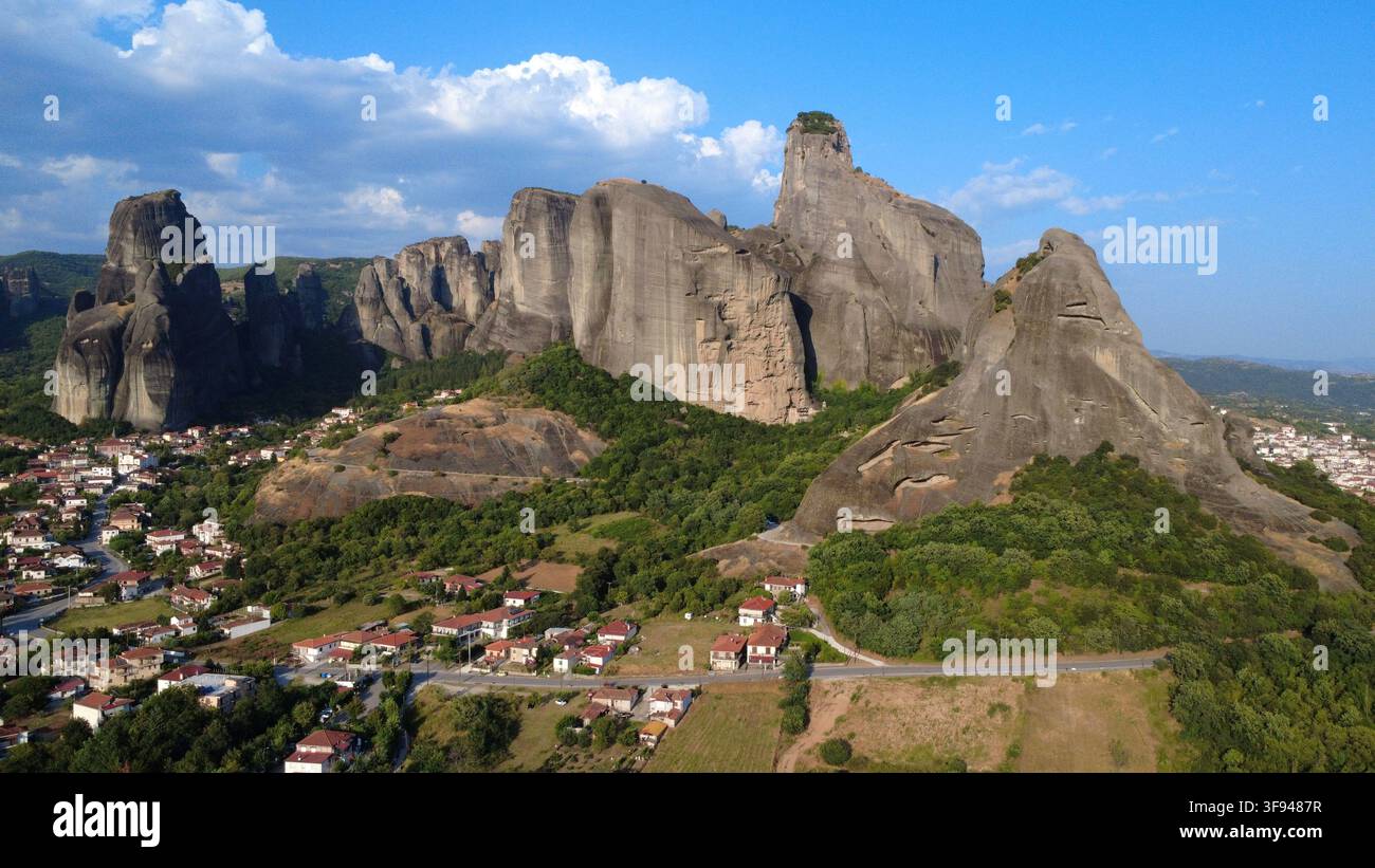 Stupenda veduta aerea degli enormi pilastri di roccia di arenaria di Meteora che si ergono sopra un villaggio tradizionale greco, incorniciati da un cielo azzurro e nuvole sparse Foto Stock