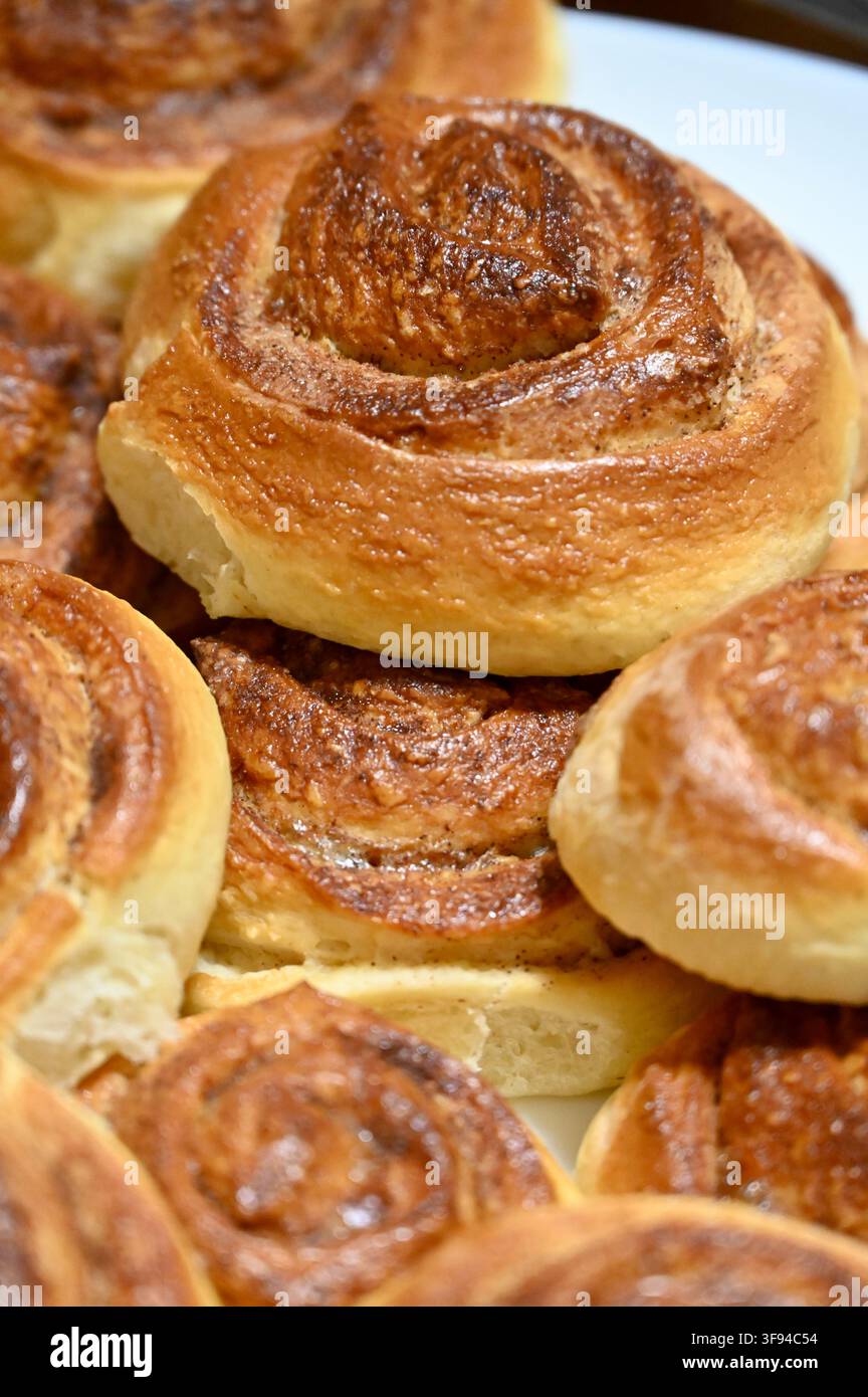 Fotografia ravvicinata commerciale di una deliziosa pila appetitosa di panini alla cannella dorati e appena sfornati impilati insieme, che mostra le loro ricche texture a spirale e le croste croccanti. Foto Stock