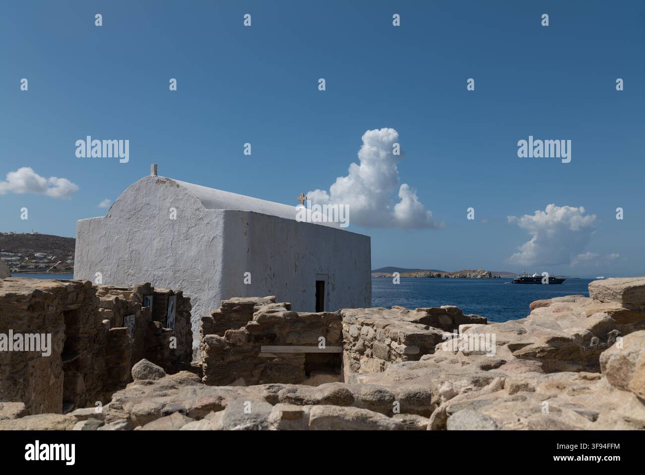 Piccola cappella imbiancata a calce che si erge sopra antiche rovine di pietra con il mare sullo sfondo, Mykonos, Grecia. Foto Stock