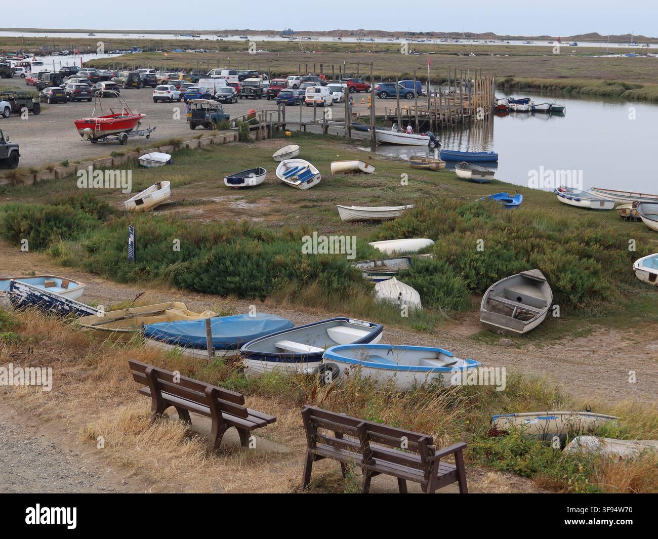 Vista del Morston Quay con il parcheggio del National Trust, barche ormeggiate nel Blakeney Channel e moli per i visitatori per salire sulle escursioni in barca per osservare i trichechi. Foto Stock