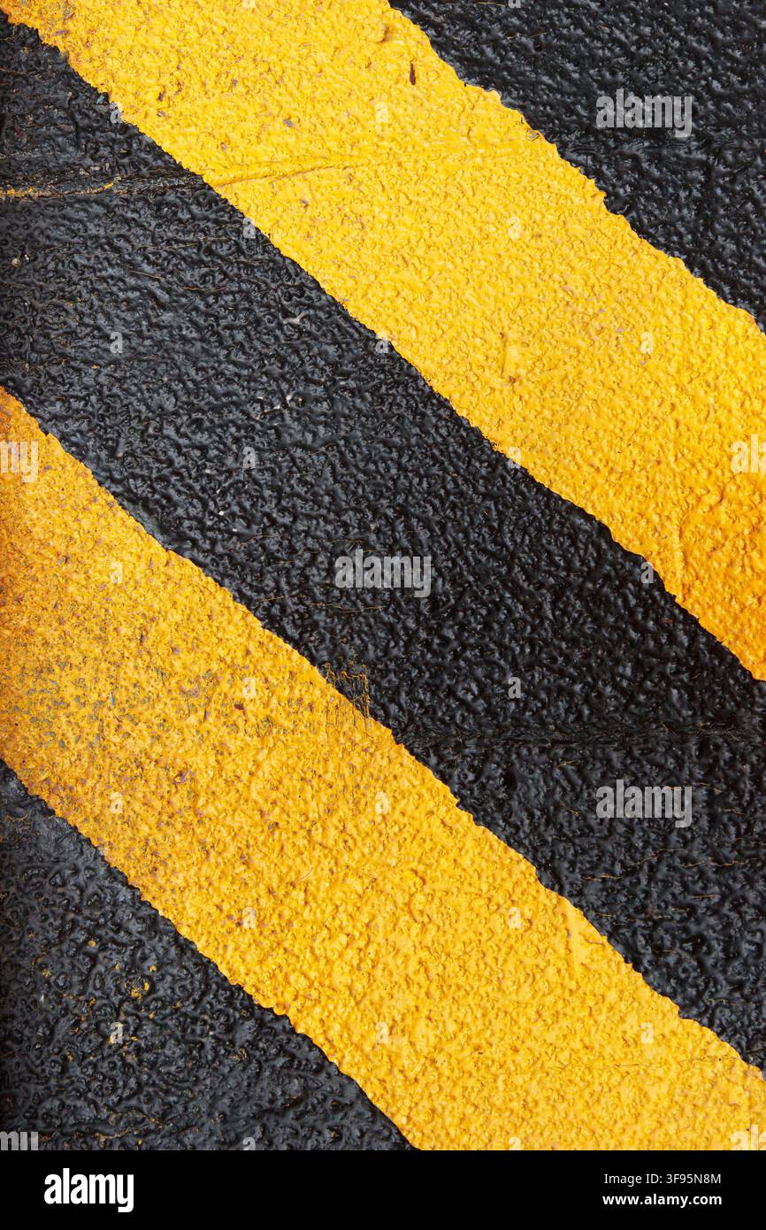Primo piano astratto di strisce di avvertimento gialle e nere dipinte su una texture ruvida di asfalto. Foto Stock