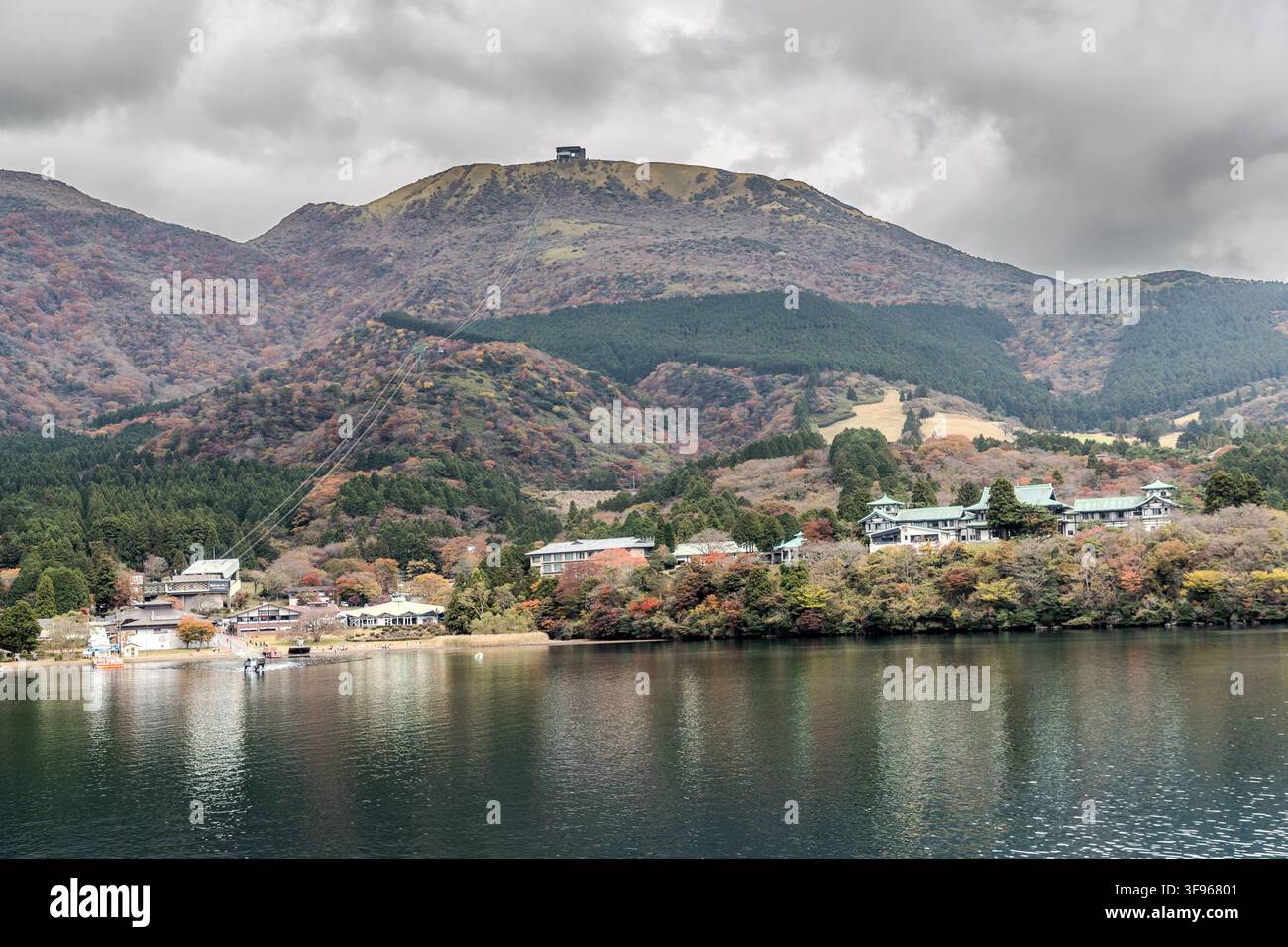 Le barche attraversano le acque del lago Ashi davanti ad edifici e una montagna boscosa vicino a Hakone, prefettura di Kanagawa, Giappone. Foto Stock