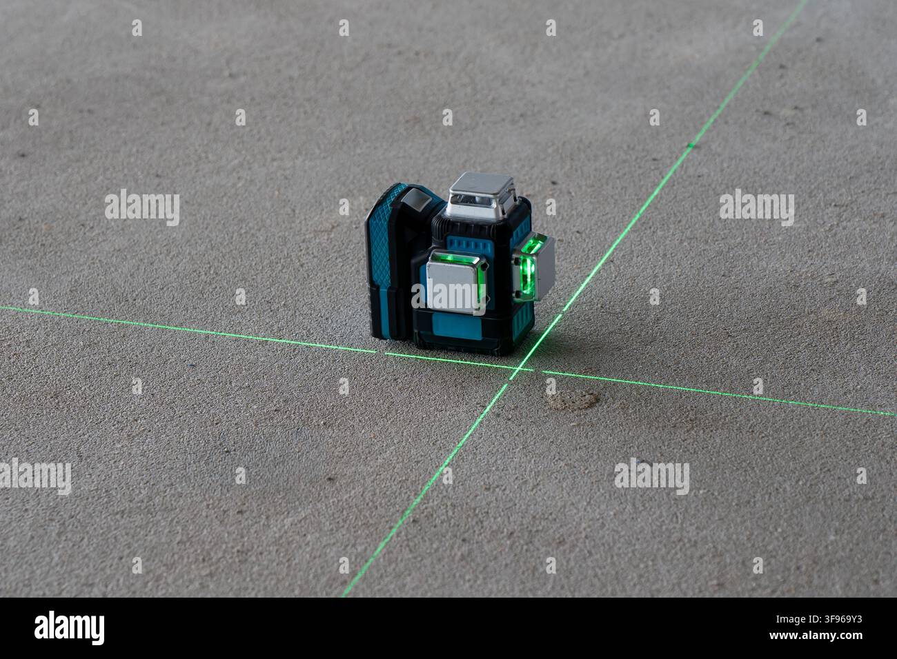 Dispositivo di livellazione laser a linea crociata verde che proietta linee di riferimento intersecanti sul pavimento di cemento durante i lavori di allineamento nella costruzione interna Foto Stock