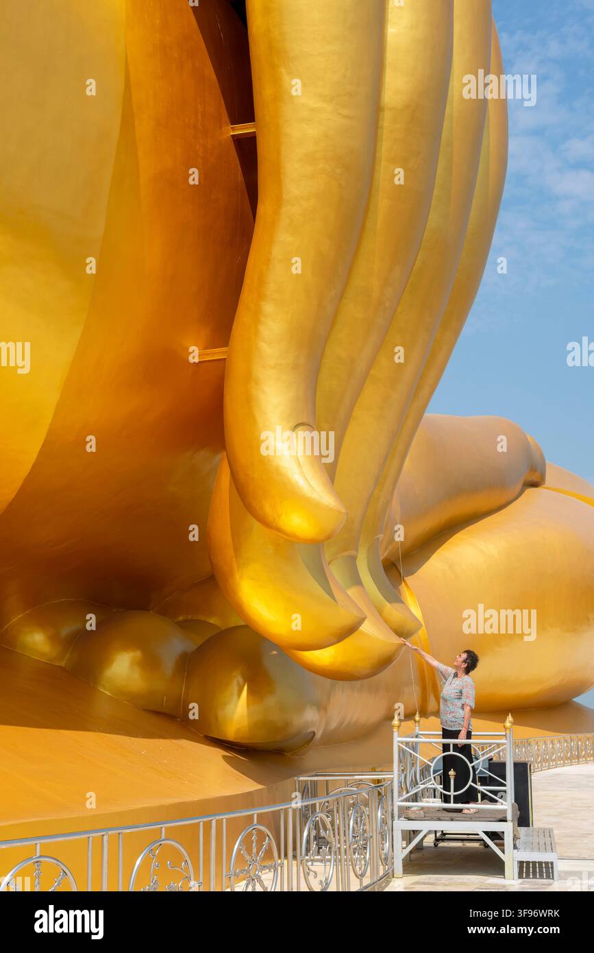 La statua di Buddha più grande della Thailandia (Luang Pho Yai), una donna di 60 anni tocca le punte delle dita della statua, poiché si crede che porti fortuna Foto Stock