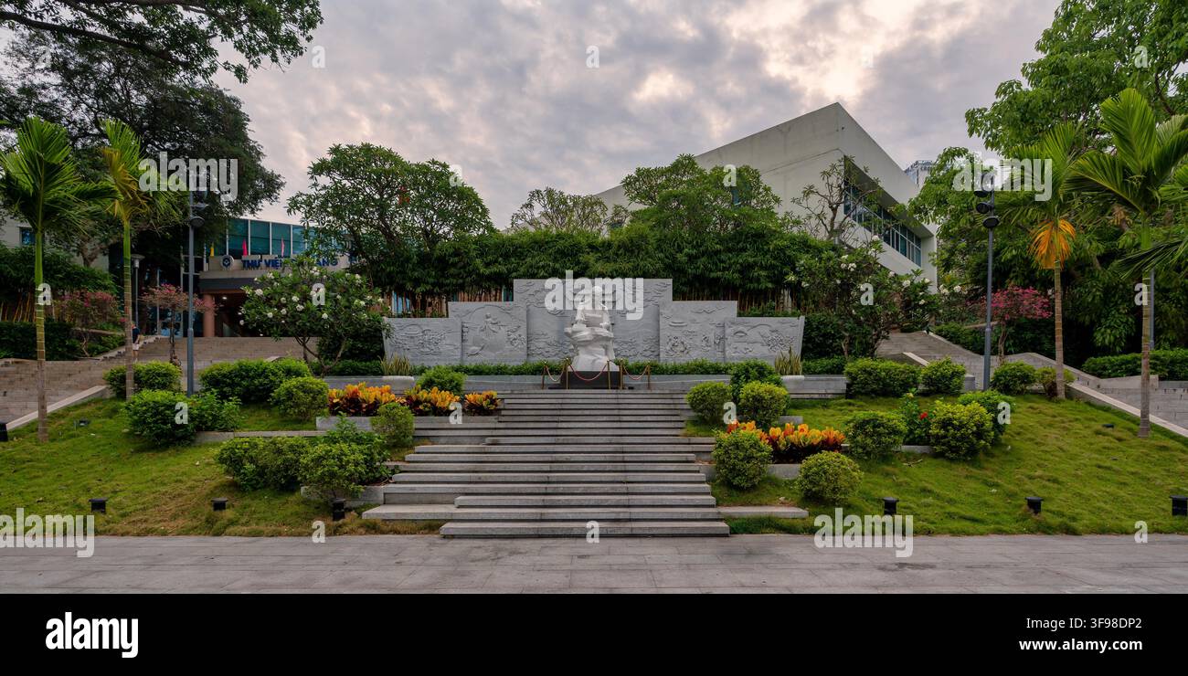 Da Nang, Vietnam - 28 aprile 2026: Statua di Ho Chi Minh davanti all'edificio della Biblioteca Generale Scientifica con un muro a rilievo in pietra e giardini paesaggistici Foto Stock