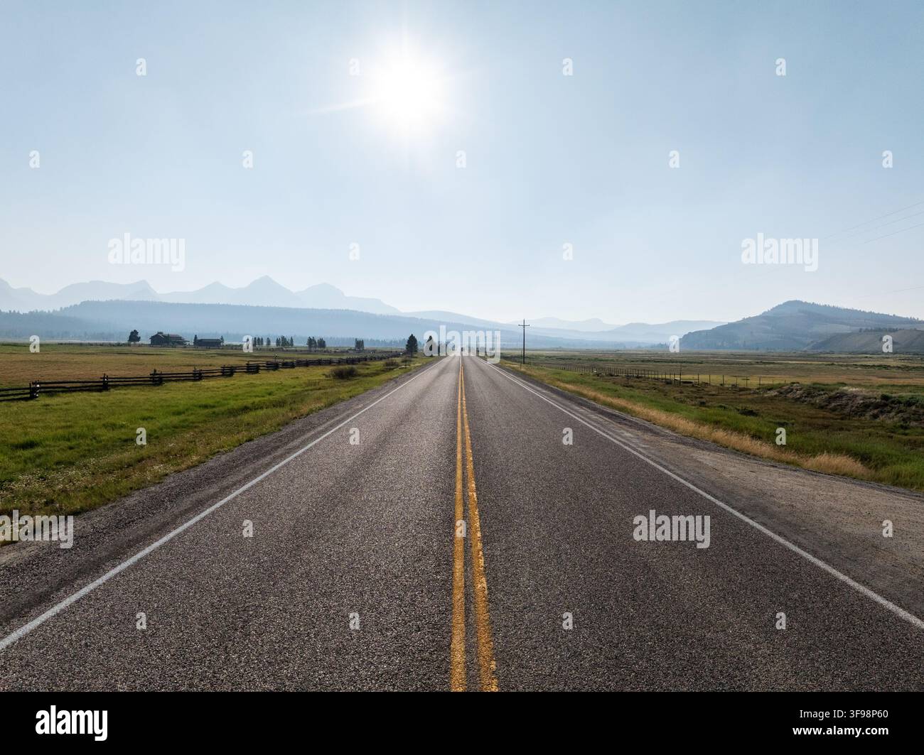 Una strada sterrata non segnalata porta a montagne lontane sotto un sole luminoso Foto Stock