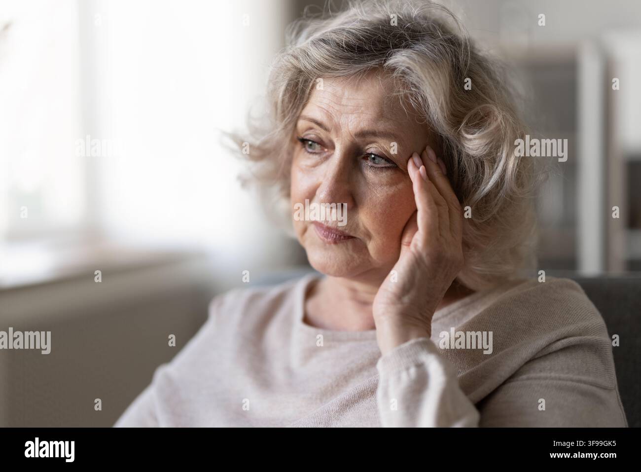 Prima piano di una donna anziana pensierosa seduta sul divano, immersa in una profonda contemplazione Foto Stock