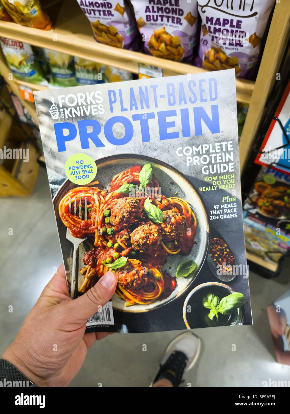 ADDISSON, TX, USA - 26 LUGLIO 2026: Una persona tiene una copia della rivista Forks Over Knives Plant-Based Protein in un corridoio del supermercato. La rivista Foto Stock