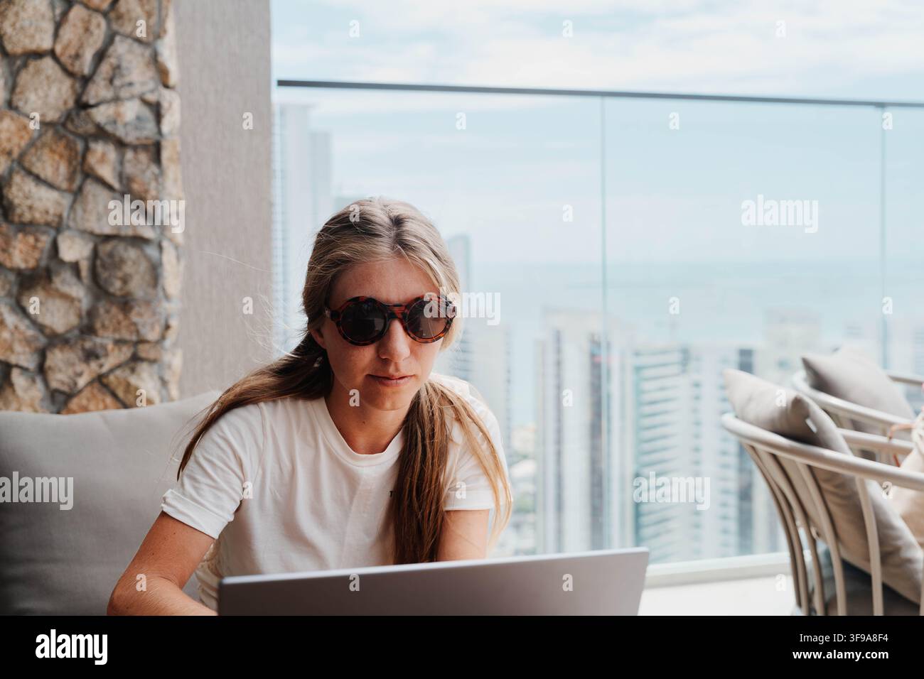 Donna che lavora su un laptop da una terrazza sul tetto con vista sulla skyline della città. Il workation unisce lavoro remoto e viaggio per flessibilità, produttività e Foto Stock