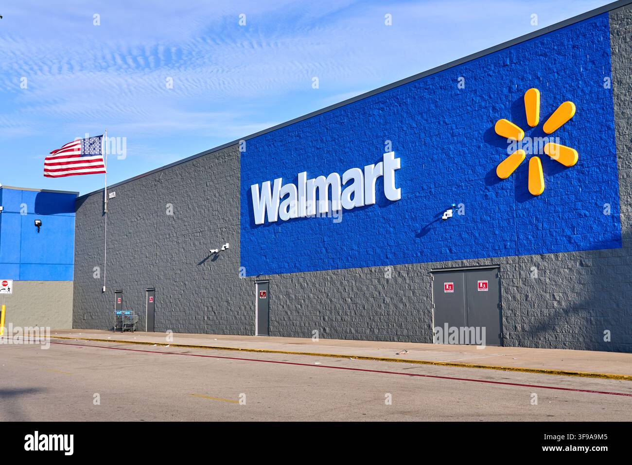 DALLAS, TX, USA - 30 LUGLIO 2026: L'esterno di un negozio Walmart mostra il suo logo sulla parete blu, accanto alla bandiera americana che sventola. W Foto Stock