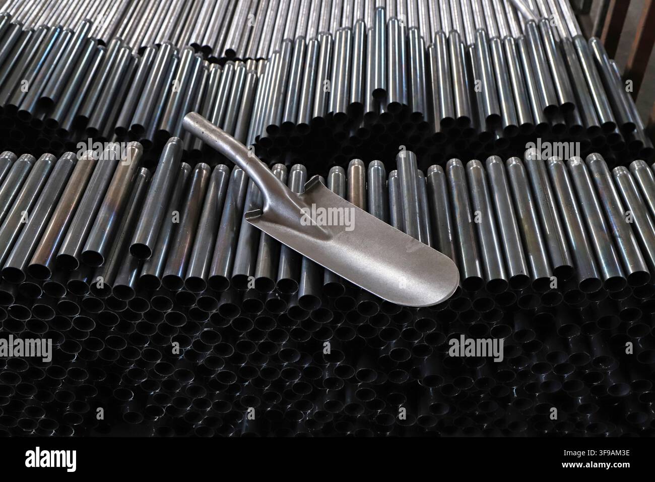 Nell'immagine, una pala di metallo formata è posizionata in modo prominente su un mucchio di materiali grezzi in tubi metallici, con tubi d'acciaio disposti densamente sullo sfondo Foto Stock