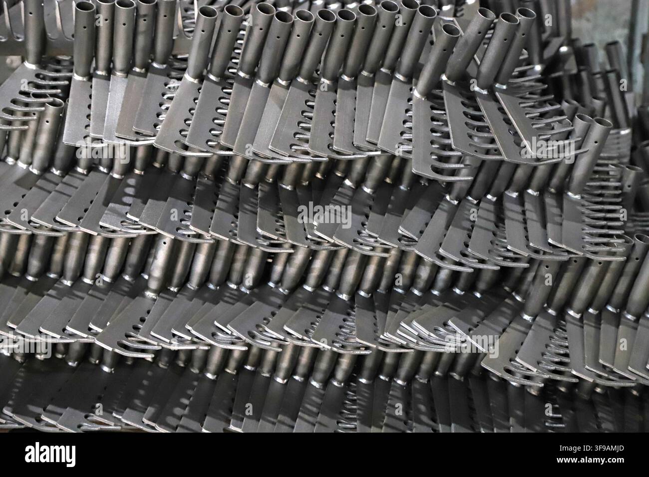 Un gran numero di semilavorati in metallo stampato è ordinatamente e densamente impilato in un laboratorio di produzione industriale. I pezzi hanno fori ritagliati mediante punzonatura Foto Stock