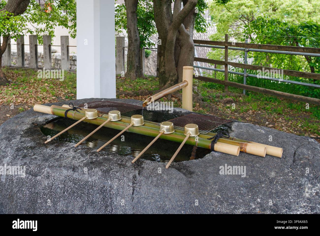 Vista dettagliata di una fontana di purificazione dell'acqua di un santuario storico con mestoli di metallo e tubi di bambù a Osaka, Giappone. Foto Stock