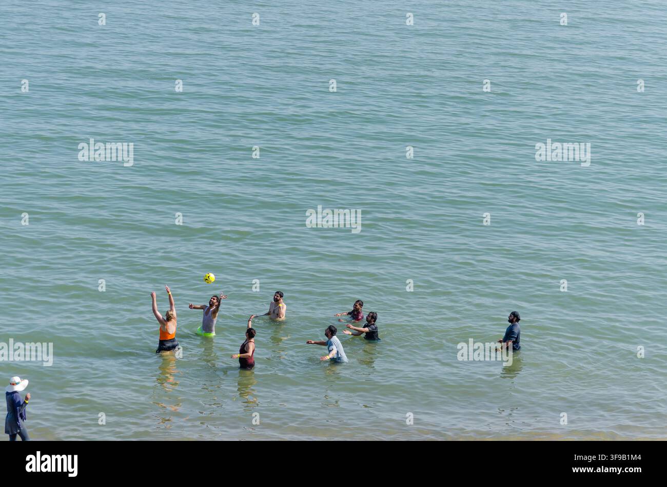 un gruppo di persone in piedi fino ai rifiuti nel mare che si lanciano una palla l'un l'altro in una giornata molto calda d'estate nel Regno Unito Foto Stock