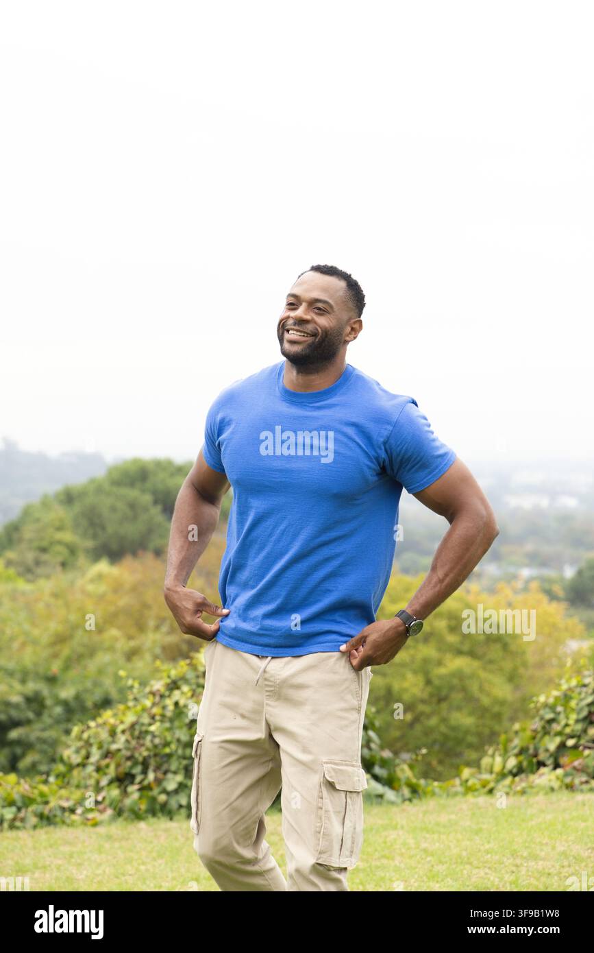 Uomo afroamericano che sistema la cintura su una collina con una maglietta blu, pantaloni cargo con tasche con patta e orologio Foto Stock
