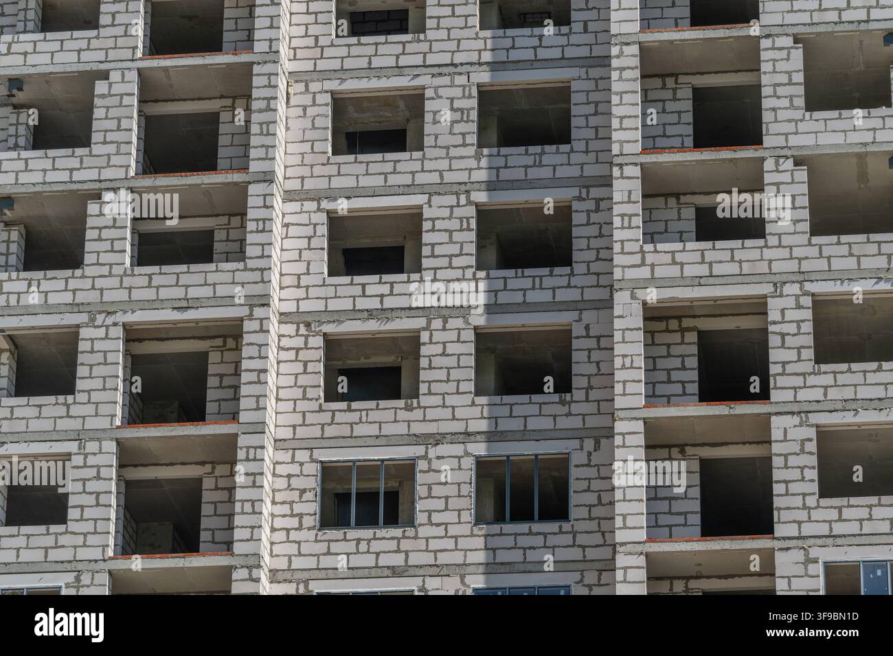 Una struttura in cemento alta si erge vuota con numerose finestre aperte in una vivace area urbana durante il giorno, evidenziando il progresso dello sviluppo urbano Foto Stock