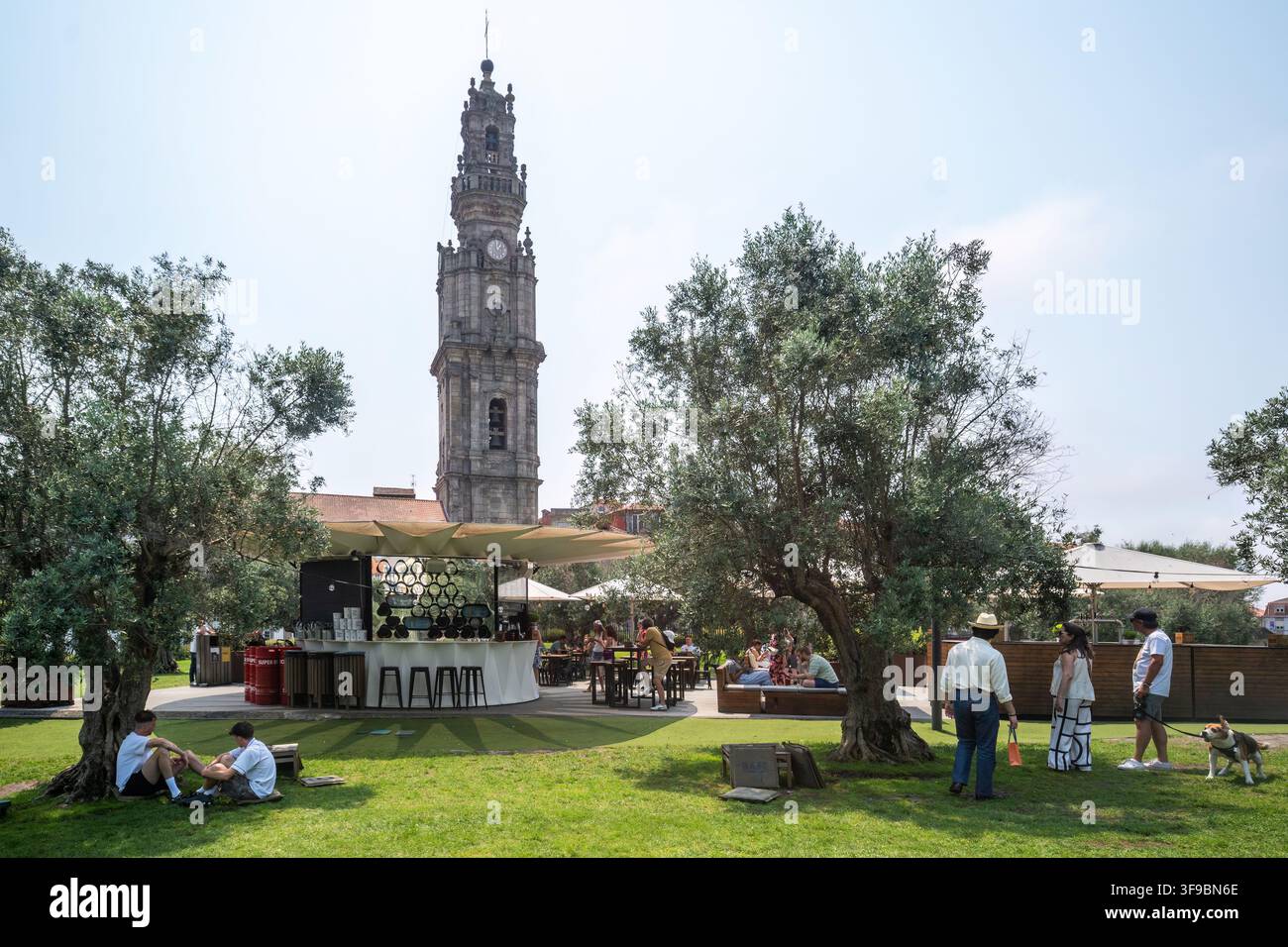 Porto, Porto, Portogallo - 29 luglio 2026: Vista della Torre dos Clerigos con persone che si rilassano nel parco, ulivi e un caffè all'aperto in una giornata soleggiata. Foto Stock