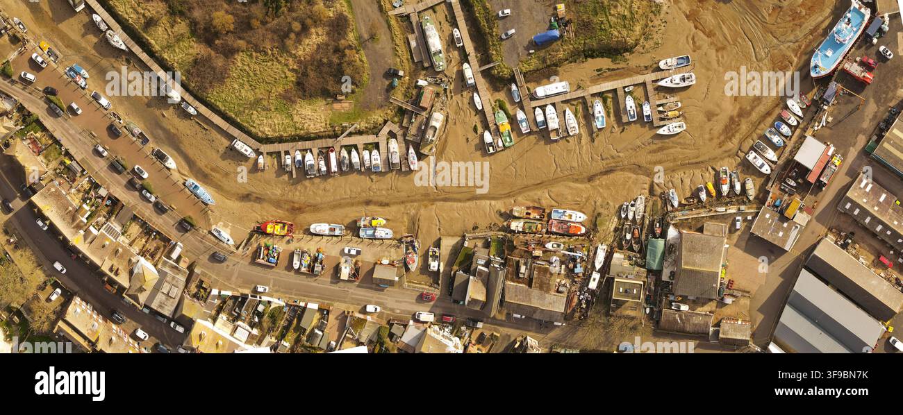 Vista aerea del porto con numerose barche arenate nel fango durante la bassa marea, circondate da edifici, strade e infrastrutture a Queenborough, Ingh Foto Stock
