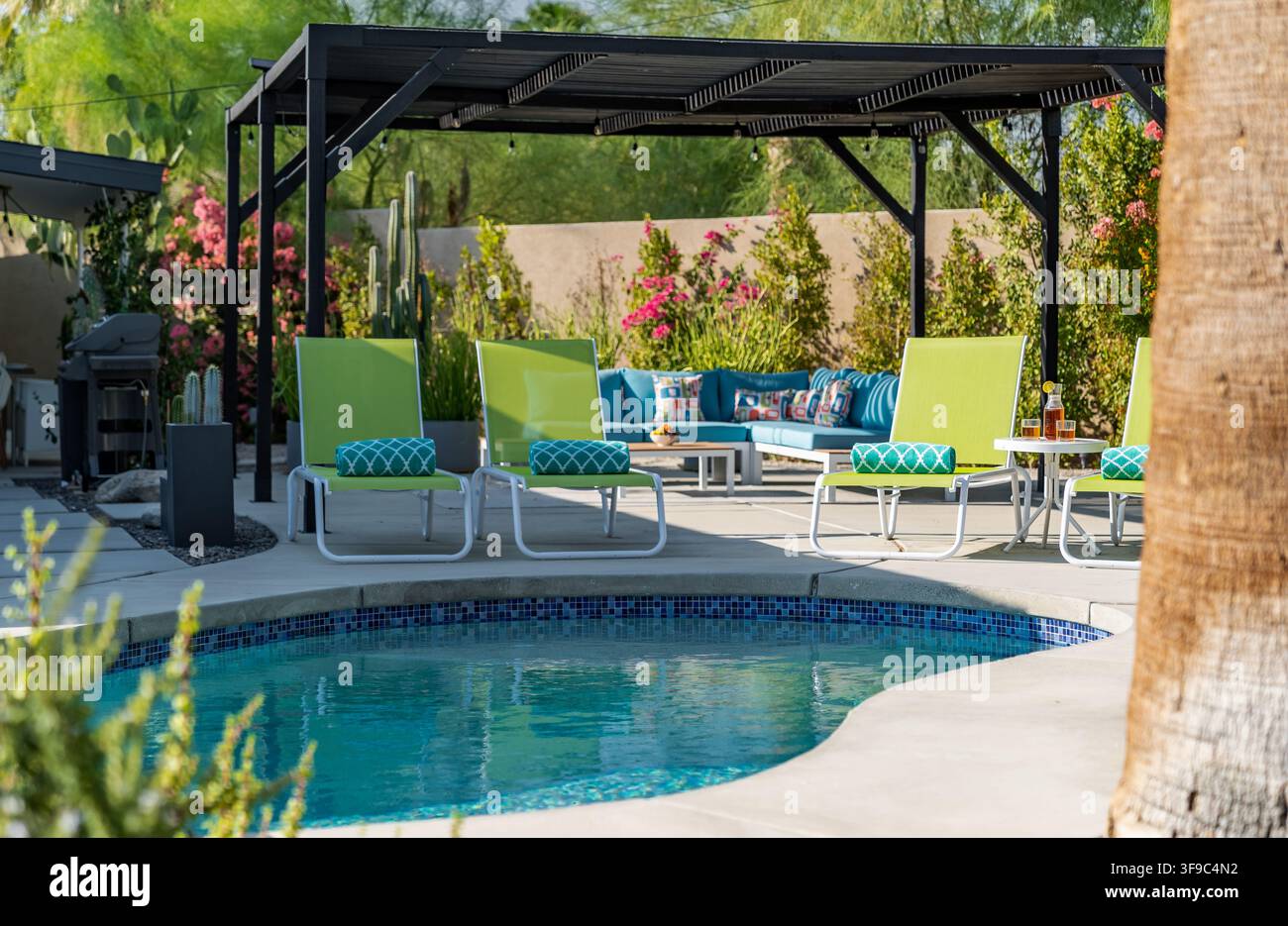 Area piscina con sedie a sdraio da patio e un lussuoso divano da esterno angolare circondato da una vegetazione desertica. Foto Stock