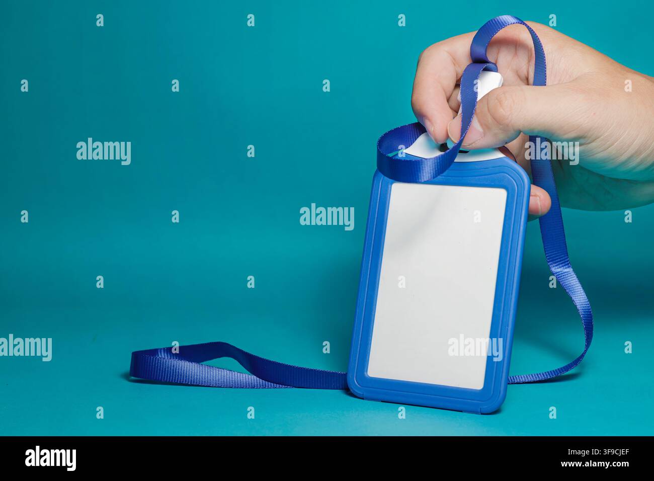 Primo piano di una mano che tiene una carta identificativa blu vuota con cordino su sfondo blu. Foto di alta qualità Foto Stock