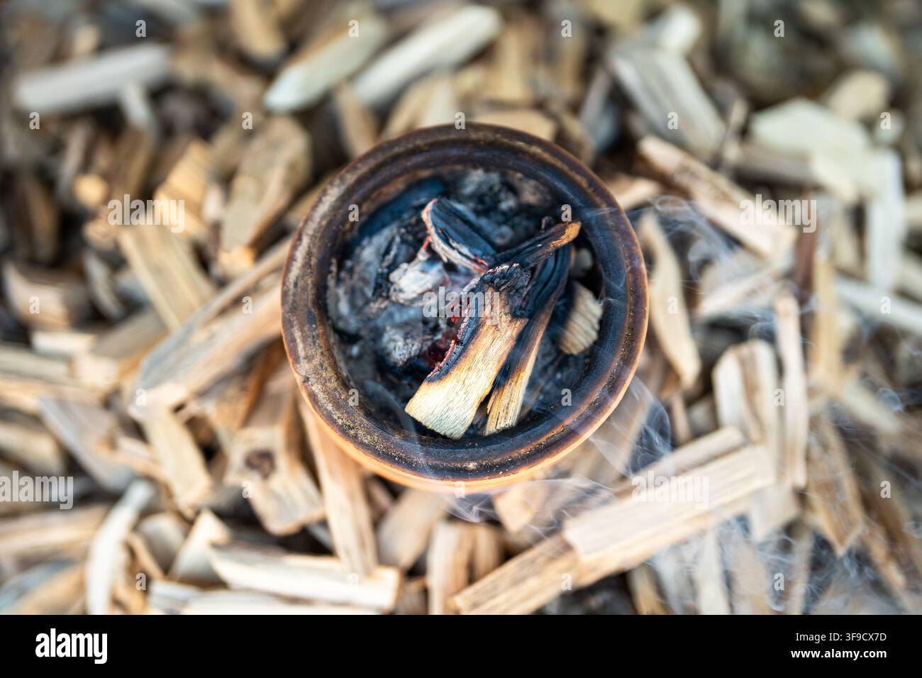 Pentola di argilla con bastoncini fumanti circondata da materiali tradizionali per la preparazione di incenso alle erbe Foto Stock
