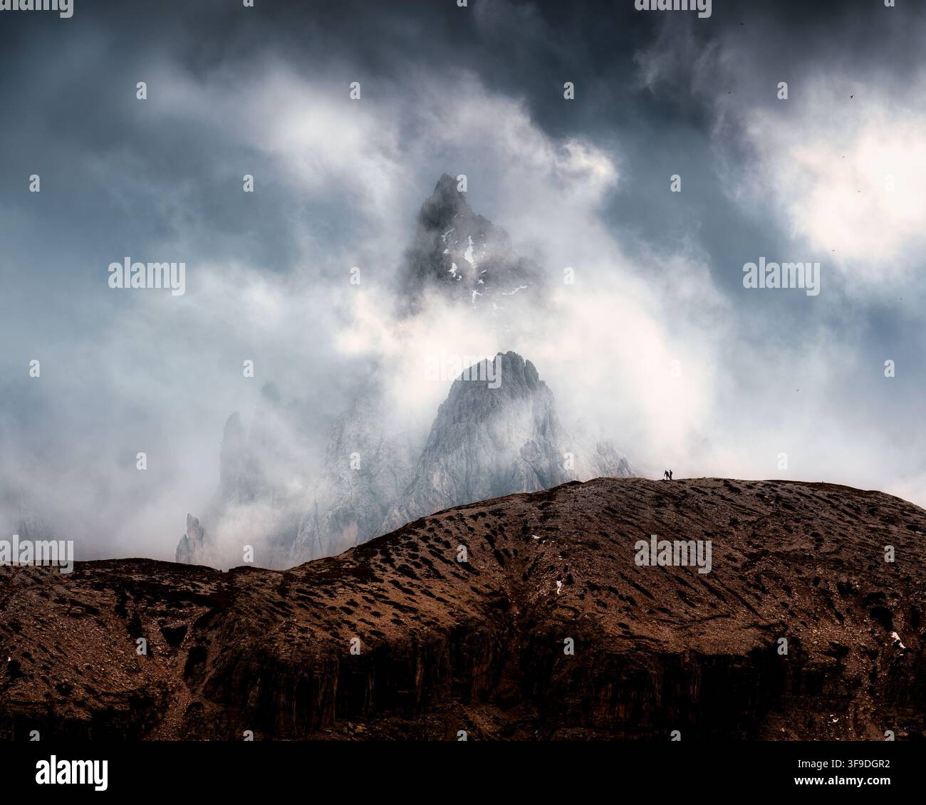 Paesaggio alpino drammatico del picco roccioso frastagliato che si eleva attraverso le nuvole di tempesta nebbiose delle Tre Cime di Lavaredo, Dolomiti, Italia Foto Stock