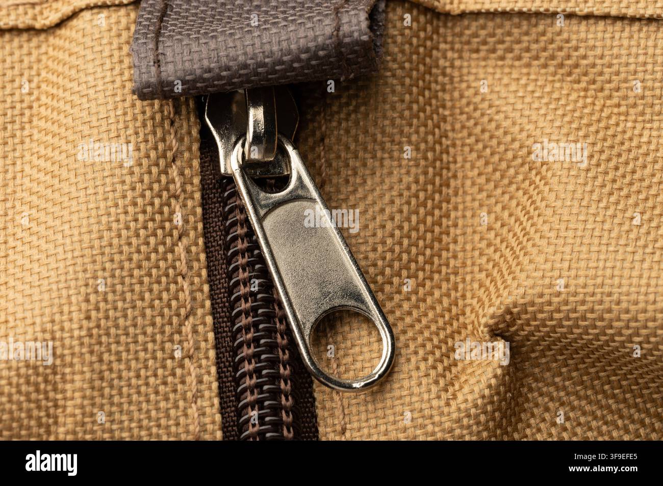 Una cerniera è mostrata su una borsa di stoffa marrone. L'immagine si concentra sulla cerniera e sui suoi dettagli. Foto Stock