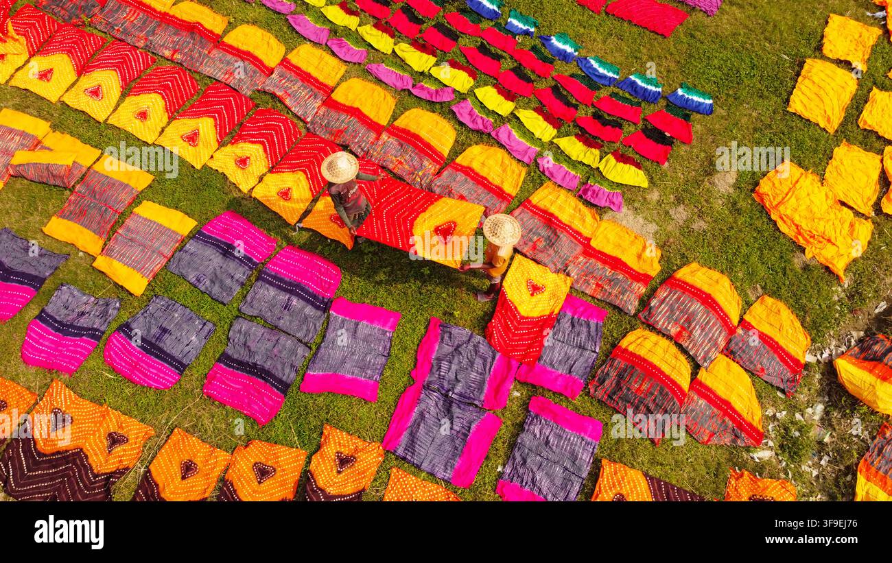 Vista aerea di tessuti colorati che si asciugano sull'erba con lavoratori che indossano cappelli di paglia a Narayanganj, Divisione di Dhaka, Bangladesh. Foto Stock