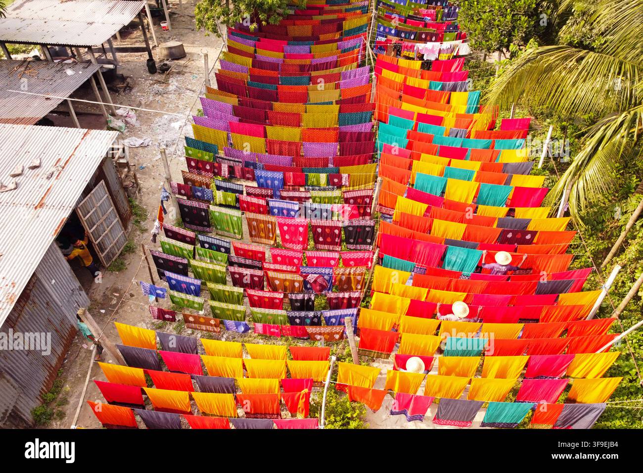 Vista aerea di tessuti colorati che si asciugano su corde in una fabbrica tessile a Narayanganj, Divisione di Dhaka, Bangladesh, con lavoratori che indossano cappelli. Foto Stock